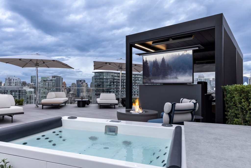 Swicks_918_Cooperage_Web-11-1797 - Swick's Landscaping Ltd. Rooftop lounge with white cushioned seating, large umbrellas, a fire pit, and a hot tub, overlooking a city skyline under cloudy skies.