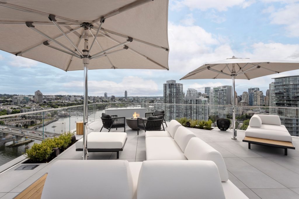 Swicks_918_Cooperage_Web-2-1687 - Swick's Landscaping Ltd. Rooftop lounge with white couches and large beige umbrellas over a city skyline at dusk.