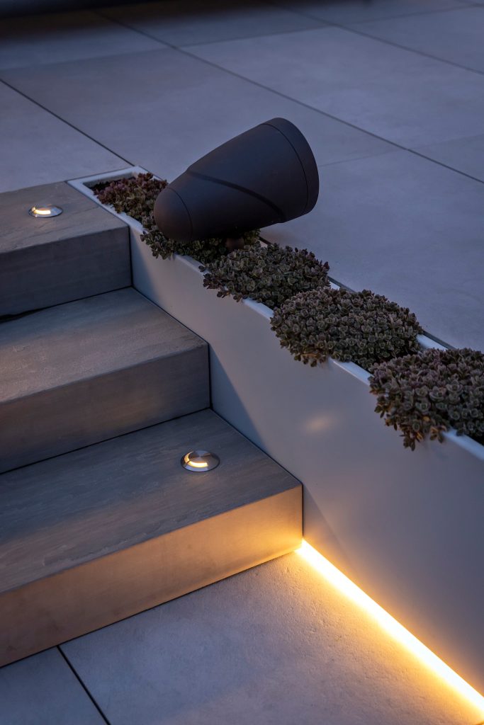 Swicks_918_Cooperage_Web-25-1927 - Swick's Landscaping Ltd. Contemporary outdoor staircase with low, warm-lit steps and a dark cone sculpture atop a planter bed of small succulents at dusk.