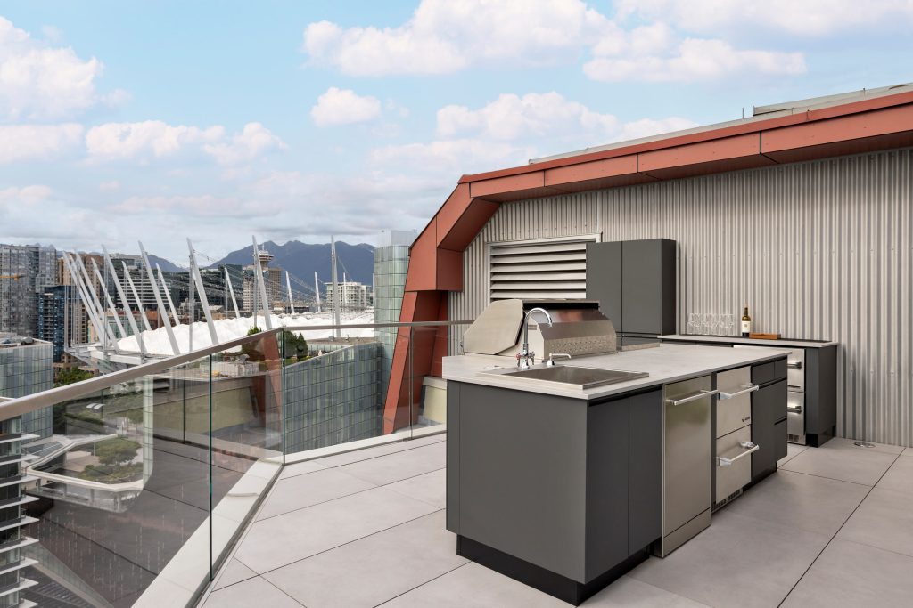 Swicks_918_Cooperage_Web-5-1714 - Swick's Landscaping Ltd. Rooftop outdoor kitchen with stainless steel grills and glass railing overlooking a city skyline.