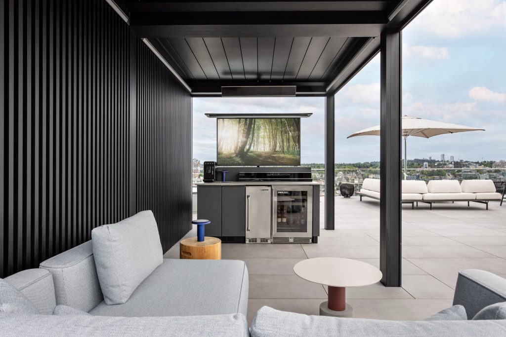 Swicks_918_Cooperage_Web-6-731 - Swick's Landscaping Ltd. Contemporary rooftop lounge with grey sectional seating, black vertical wall slats, and a built-in grill; city skyline in the distance.