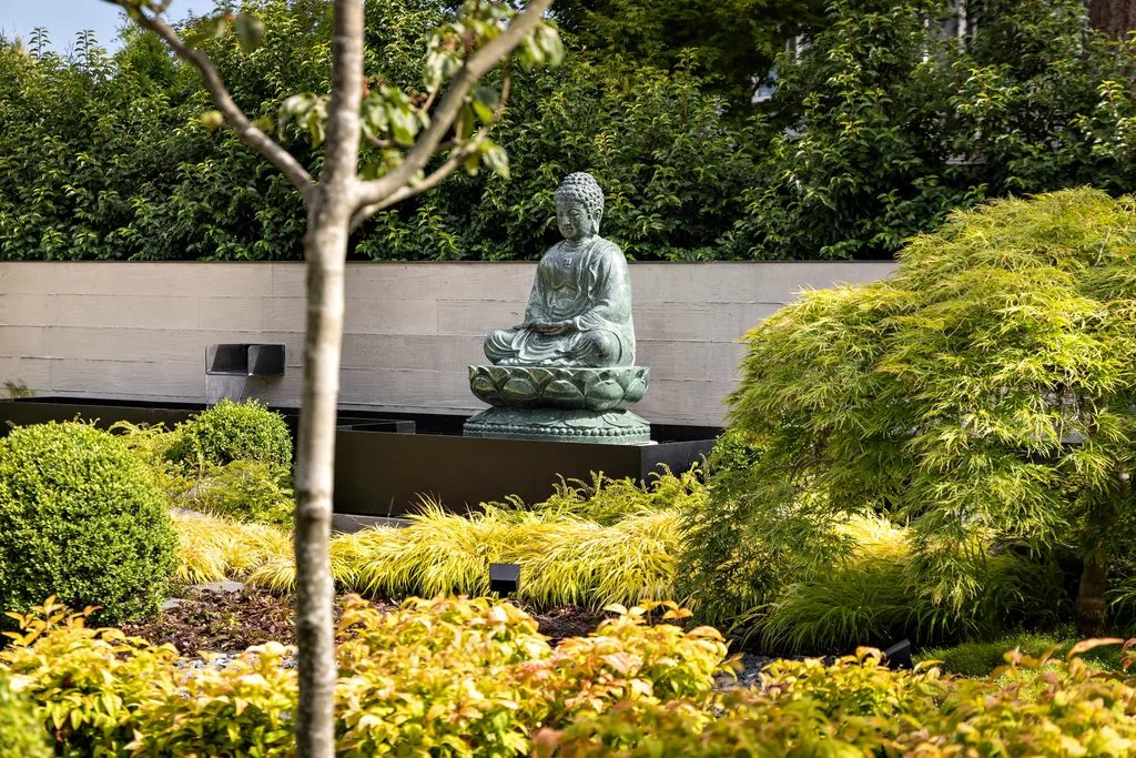 Swicks_4280_River_Web-10-7986 - Swick's Landscaping Ltd. Stone Buddha statue seated in a garden, surrounded by green hedges and yellow ornamental grass