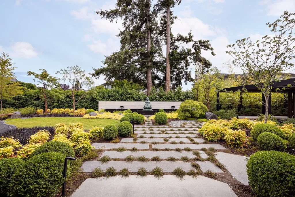 Swicks_4280_River_Web-25-2476 - Swick's Landscaping Ltd. Tranquil Japanese-style garden with stone stepping path, trimmed shrubs, and a small Buddha statue at center.