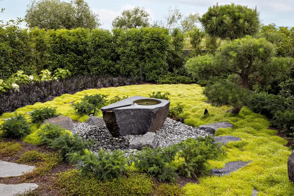 Swicks_4280_River_Web-34-2495 - Swick's Landscaping Ltd. Stone basin fountain in a Japanese-style garden, surrounded by moss, rocks, and dense greenery.