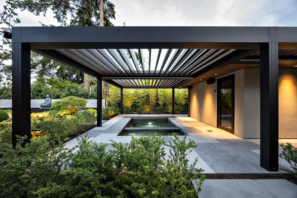 Swicks_4280_River_Web-42-2535 - Swick's Landscaping Ltd. Modern black pergola with slatted roof over a sculpture garden and rectangular reflecting pool; exterior lighting highlights beige walls at dusk/early evening.