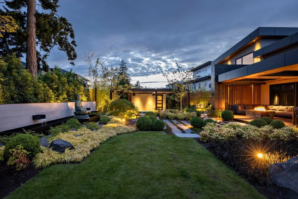 Swicks_4280_River_Web-52-2569 - Swick's Landscaping Ltd. Modern house with outdoor lounge, warm yard lights, and a Buddha statue in a landscaped garden at dusk