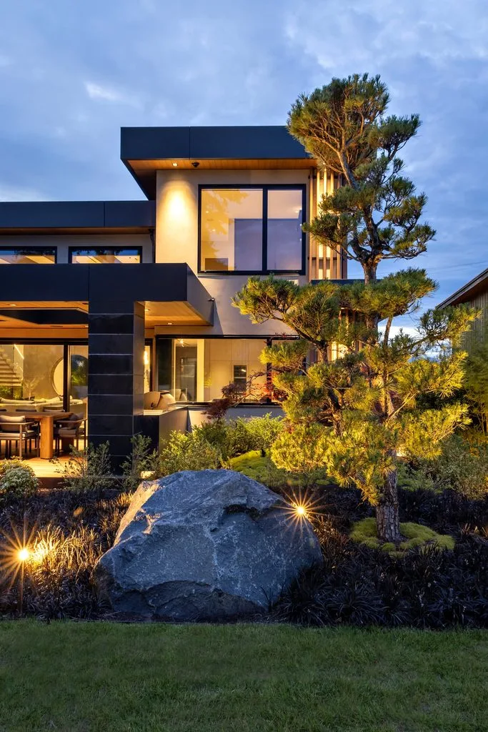 Swicks_4280_River_Web-54-8133 - Swick's Landscaping Ltd. Modern two‑story contemporary house with large windows and warm interior lighting, set in a landscaped yard at dusk, with a tall pine tree nearby.