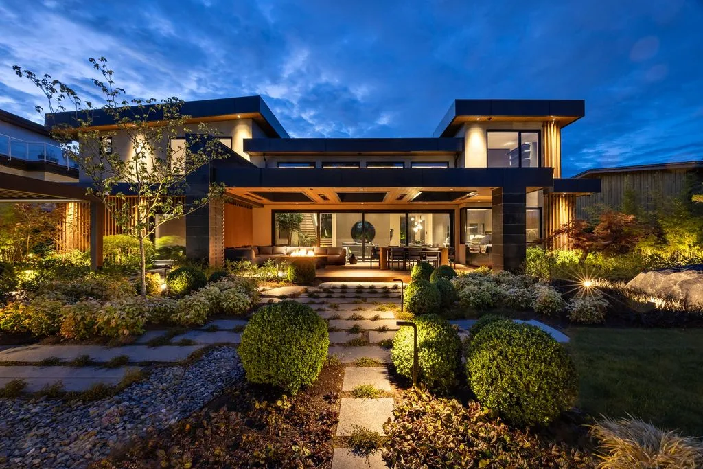 Swicks_4280_River_Web-60-2583 - Swick's Landscaping Ltd. Modern two-story house with outdoor living area illuminated at dusk, surrounded by a manicured garden and stepping-stone path.