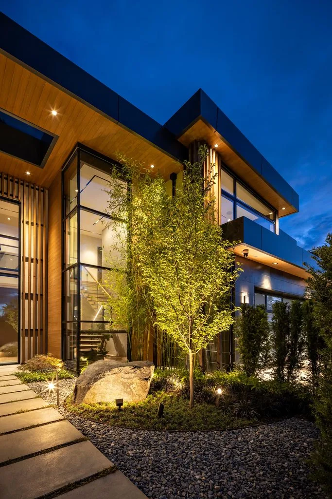 Swicks_4280_River_Web-64-8183 - Swick's Landscaping Ltd. Modern, angular house exterior at dusk with warm lighting, glass walls, wooden accents, and landscaped pebble garden.