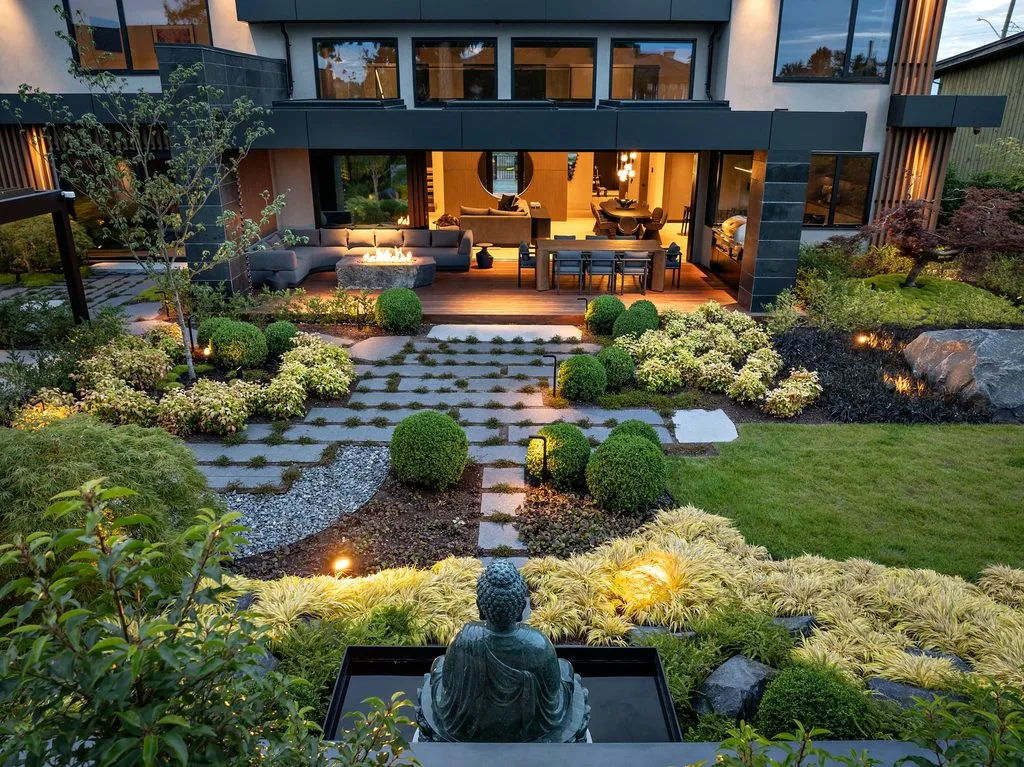 Swicks_4280_River_Web-85-0371 - Swick's Landscaping Ltd. Outdoor modern home with backyard living area featuring a circular fire pit, grey sectional sofa, and a long dining table under a glass-walled house.
